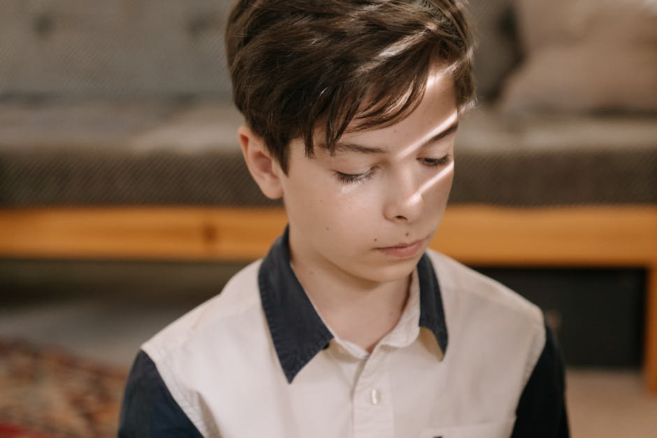 A young boy indoors bathed in natural sunlight, looking reflective and calm.
