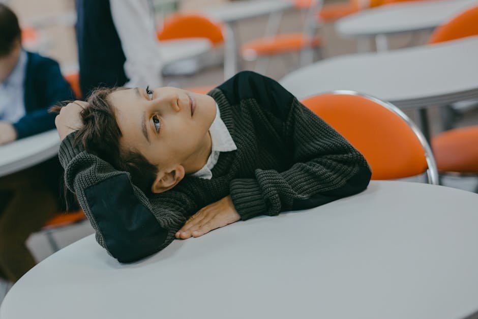 A young boy in a cozy sweater leans on a table, looking thoughtful in an indoor setting.