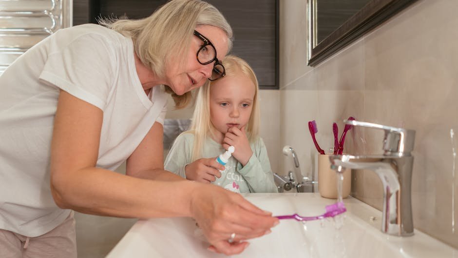 Grandmother helps granddaughter with tooth brushing routine in bathroom.
