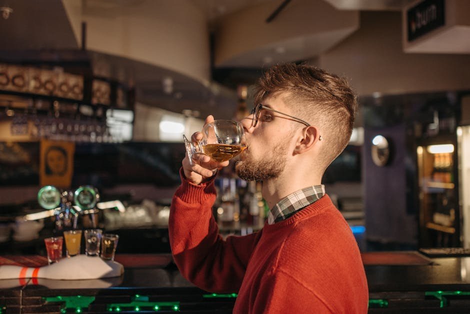Young man savoring a drink in a stylish bar setting, surrounded by warm lighting.