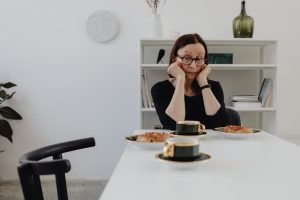 Elderly woman feeling lonely and contemplative at a dining table with coffee and pastries.