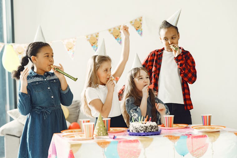 Group of kids enjoying a fun birthday party indoors with cake and party hats.