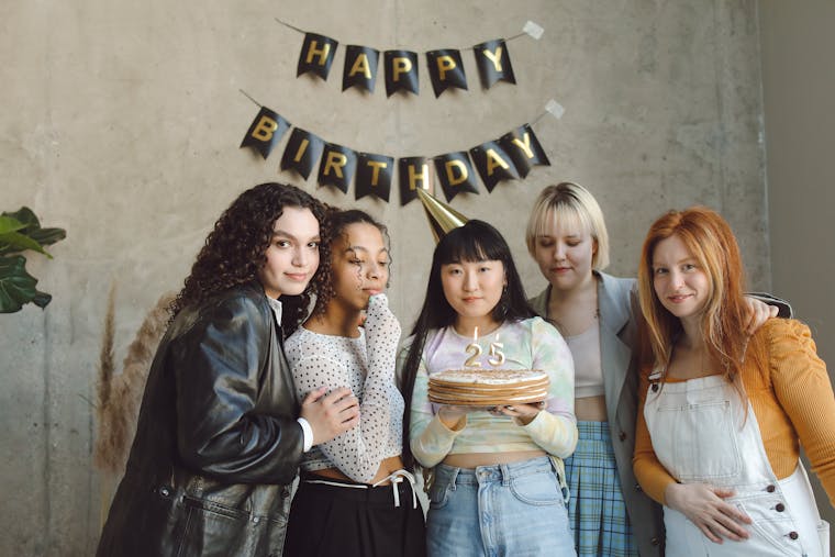 Group of friends celebrating a 25th birthday indoors with cake and decorations.