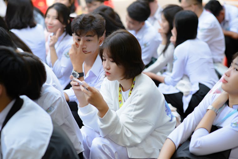 Group of students sitting outdoors, using smartphones and engaging with technology.