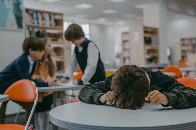 A child sits alone in a school library, highlighting themes of bullying and isolation.