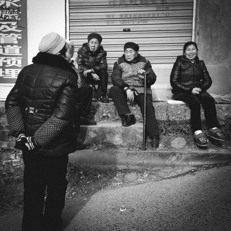 A group of elderly people in winter clothing socializing on urban street stairs.