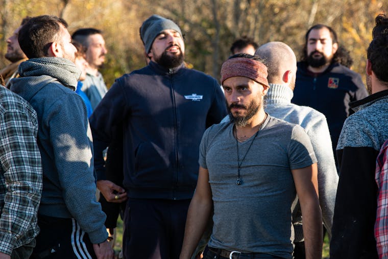 A diverse group of adults standing closely in an outdoor setting, interacting with focus.