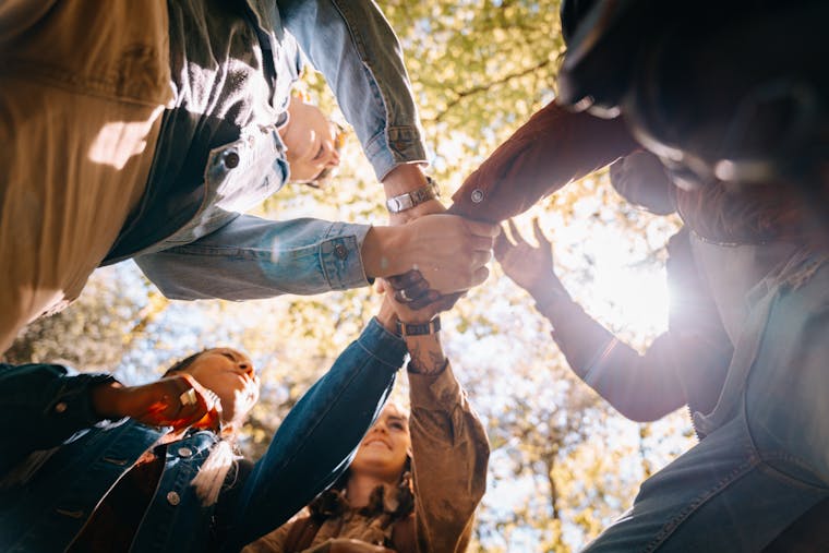 A diverse group of adults holding hands in unity and friendship under daylight.