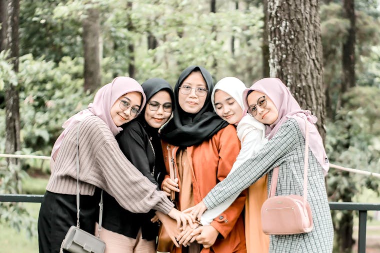 A group of women embracing in a friendly pose in a lush green forest setting.