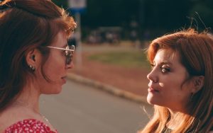 Two women face each other outdoors, engaged in conversation during a warm sunset.