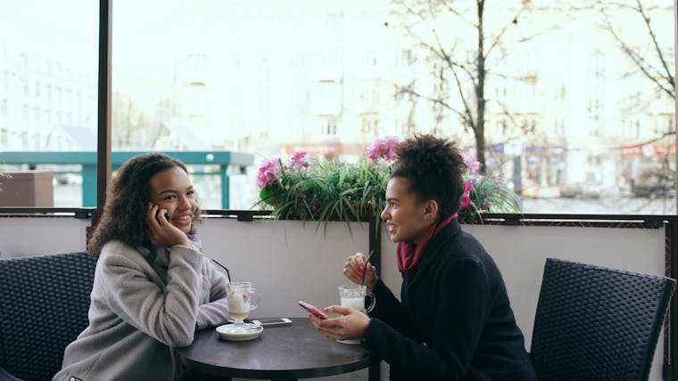 Two women enjoying coffee and chatting at an outdoor cafe setting.