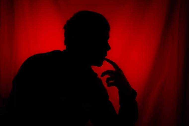 A moody silhouette of a person deep in thought against a striking red background.