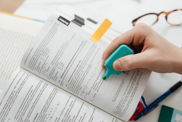 Close-up of a hand using a highlighter on an open textbook, focusing on key information.