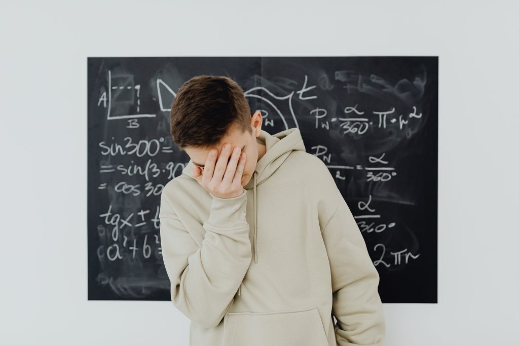 A frustrated student in a classroom standing in front of a blackboard filled with trigonometry equations.