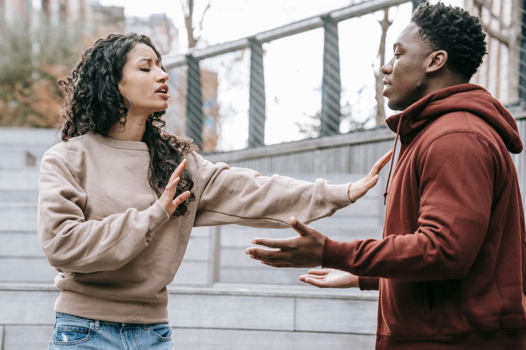 Side view of ethnic woman with outstretched arms trying to stop African American man while breaking up on street in city