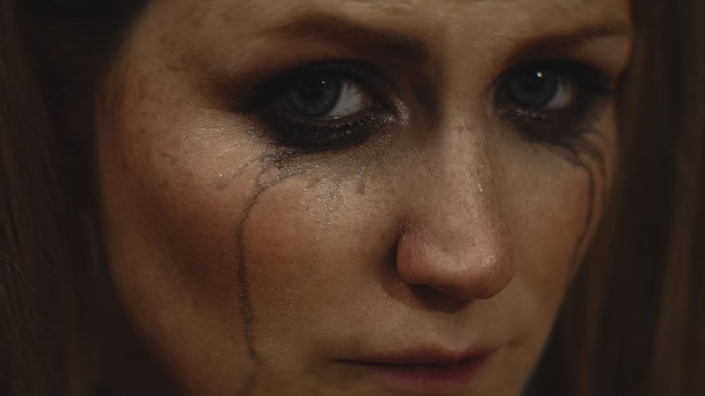 Close-up of a woman with smeared makeup and tears on her face showing deep emotion.