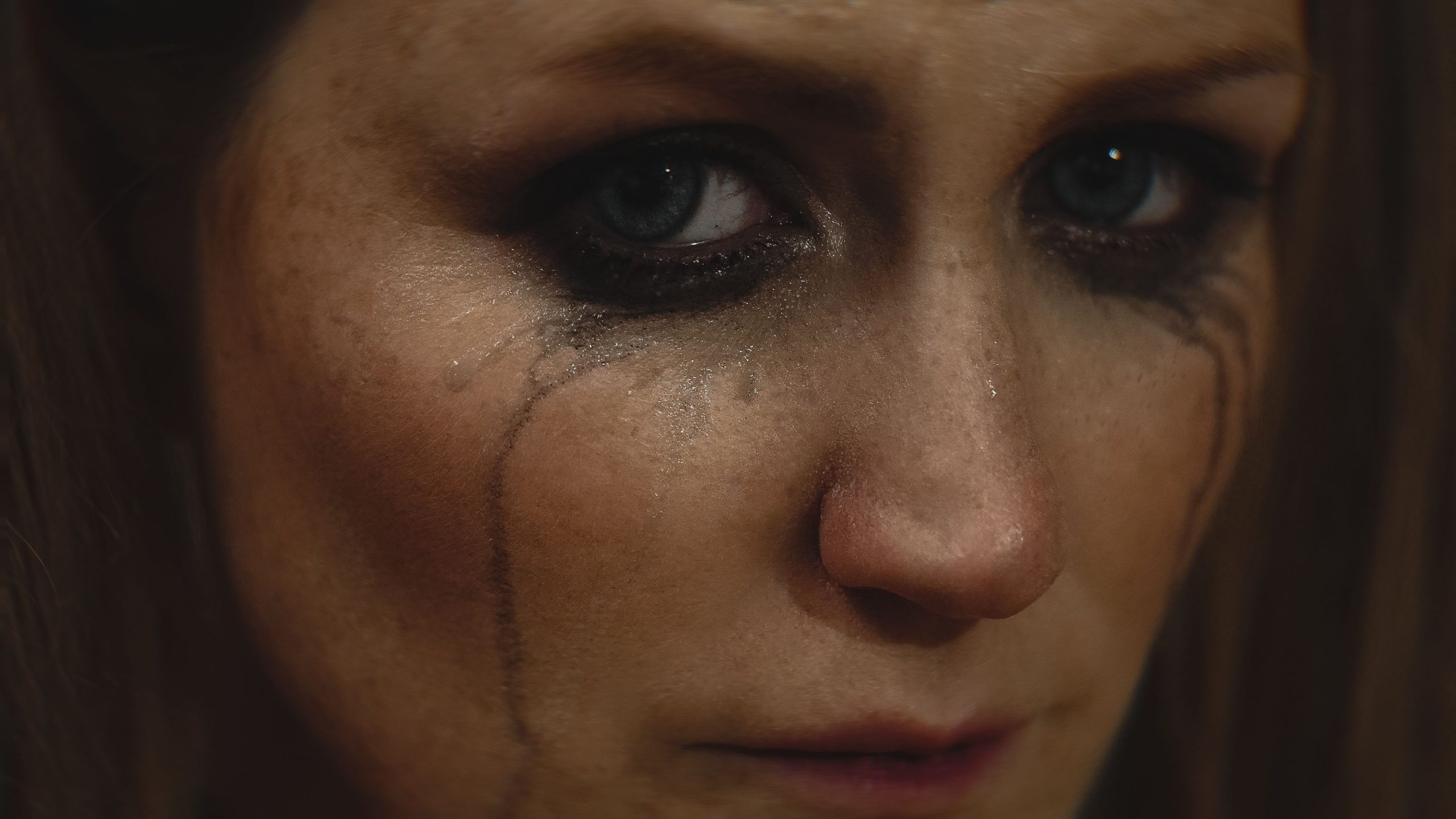 Close-up of a woman with smeared makeup and tears on her face showing deep emotion.